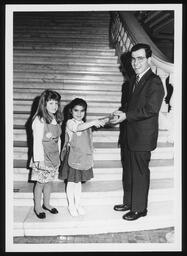 Rep. Thomas Scrimenti is handed a box of girl scout cookies by two girl scouts. Standing on the main rotunda steps.